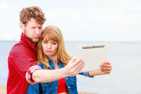 Technology holidays and happiness concept. Young couple taking self picture selfie with tablet outdoor on by seasideの写真素材