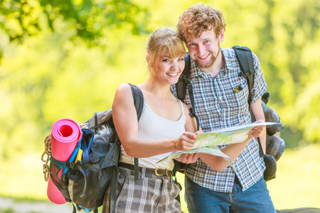 Man and woman tourists backpackers reading map on trip. Young couple hikers searching looking for...