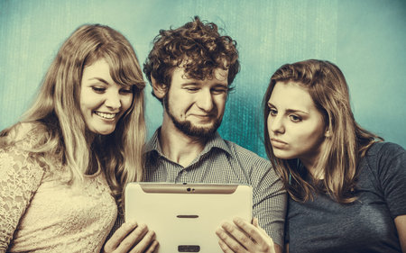 Friends browsing surfing internet on tablet. Young people man guy and women girls sitting on sofa...