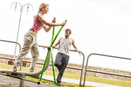 Active woman exercising on elliptical trainer machine and man listening to music. Fit sporty girl in...