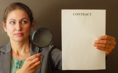 Contracts and agreements concept. Adult beauty woman in jacket holding showing contract. Close up portrait of person with loupe studying agreement.の写真素材