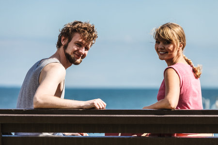 Couple man and woman dating by sea ocean outdoor. Young girl and guy sitting on bench. Summer love.