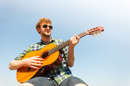 Young man hipster playing guitar. Handsome guy in sunglasses relaxing on summer vacation.