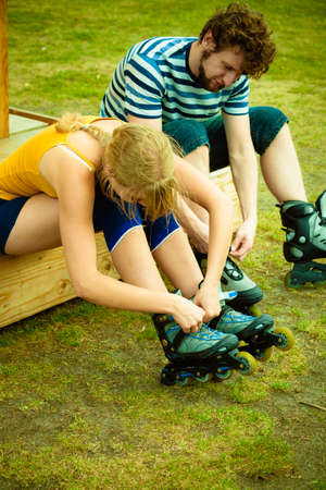 Couple skating in park. People friends putting on roller skates. Woman and man in outdoor fitness activities.の写真素材