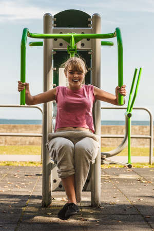 Active young woman exercising on chest press machine. Strong girl in training suit working out at outdoor gym. Sport fitness and healthy lifestyle concept.の写真素材