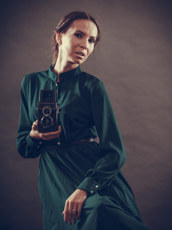 Woman retro style long dark gown taking picture with old camera, vintage photo