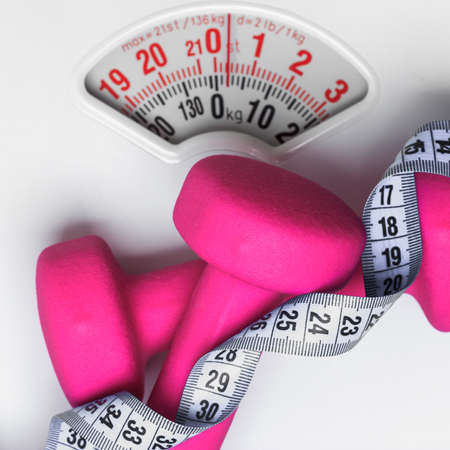 healthy lifestyle fitness weight control concept. Closeup pink dumbbells with measuring tape on white scalesの写真素材