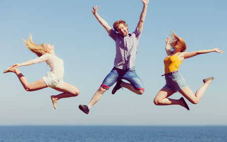 Friendship freedom summer holidays concept. Group of friends boy two girls jumping outdoor against...