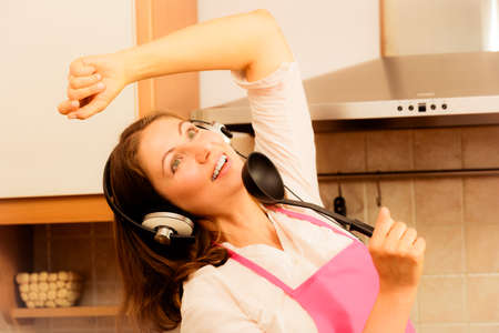 Cooking preparing and making food concept. Modern beauty woman housewife cook chef wearing pink apron listening music on earphones singing and dancing in kitchen.の写真素材