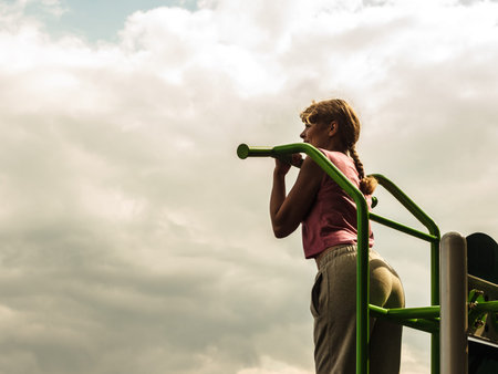 Strong active woman in training suit exercising working out at outdoor gym. Sport fitness.