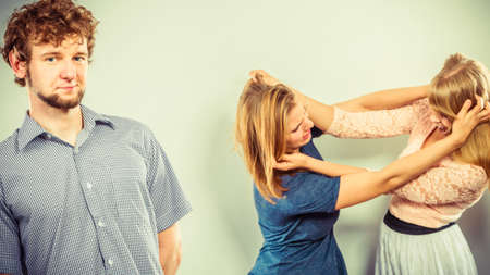 Aggressive mad women fighting over man. Young jealous girls wooing guy. Violence.の写真素材