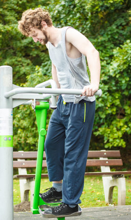 Active young man exercising on ski trainer machine. Muscular sporty guy in training suit working out...