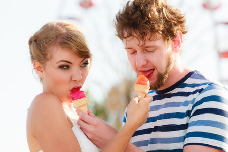 Summer holidays and happiness concept. Young couple eating ice cream outdoor in amusement park ferris wheel in the backgroundの写真素材