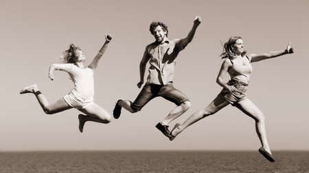 Carefree young friends people jumping by sea ocean water. Happy women and man having fun. Summer happiness and freedom.の写真素材