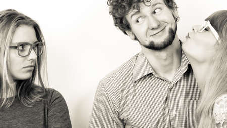 Jealousy and betrayal concept. Abandoned jelous girl watching on happy couple - young attractive blondie woman kissing handsome boy.の写真素材