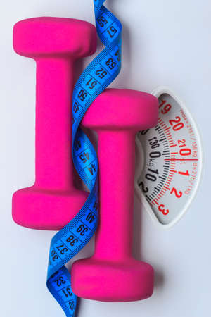 healthy lifestyle fitness weight control concept. Closeup pink dumbbells with blue measuring tape on white scalesの写真素材