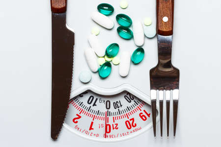 Pills with knife fork on dish white scalesの写真素材