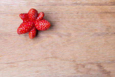 Red odd single strawberry fruit on wooden table board copy space text areaの写真素材