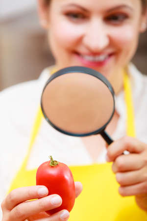 Mature woman female inspecting testing tomato food with magnifying glass.の写真素材