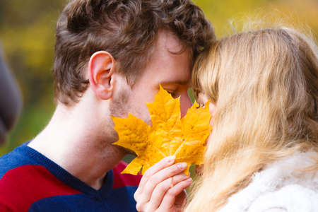 Love relationship dating and people concept - close up couple hiding behind maple leaf kissing in autumn parkの写真素材