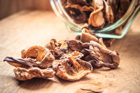 Closeup dry mushrooms spilling out from storage jar on wooden surface table background.の写真素材