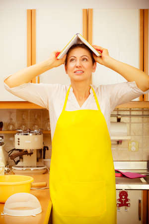 Funny housewife cook with cookbook on head in kitchen.の写真素材