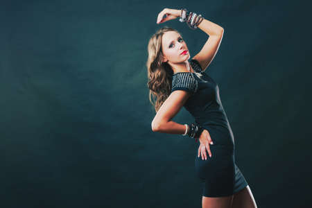Pretty young woman wearing multiple bracelets jewellery necklace in black elegant evening dress on darkの写真素材