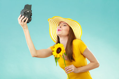 Summer woman wearing yellow dress and hat with sunflower taking self picture with old vintage camera...