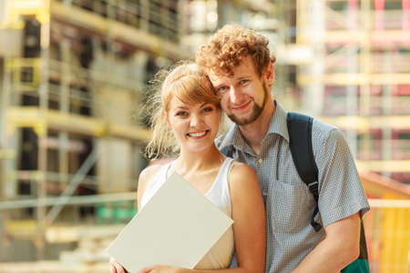 Real estate and family concept - young couple looking at blueprint project  building plans dreaming about new house in modern residential area, construction site in the backgroundの写真素材