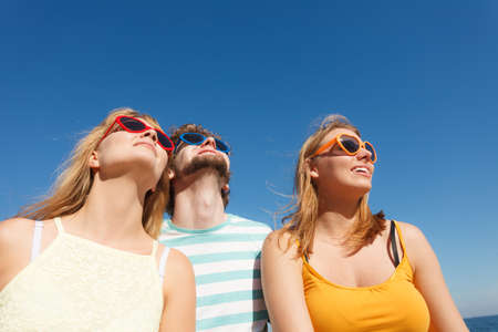 Friendship happiness summer holidays concept. Group of friends boy two girls in colorful sunglasses having fun outdoor against sky.の写真素材