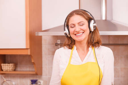 Cooking and preparing food concept. Happy relaxed beauty woman housewife chef with earphones listening music in house kitchen making dinner meal.の写真素材