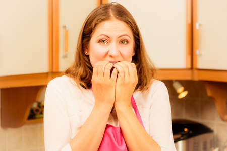 Frightened and worried woman wearing pink apron. Unhappy anxious and stressed housewife in kitchen. Negative facial emotion. Filteredの写真素材