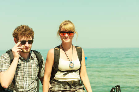 Two young people tourists hiking by sea ocean water. Backpackers couple on summer vacation trip journey.の写真素材