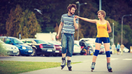 Holidays, active people and friendship concept. Young fit couple on roller skates riding outdoors, woman and man rollerblading together on city streetの写真素材