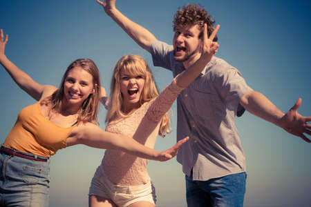 Friendship happiness summer holidays concept. Group of friends boy two girls having fun outdoor stretching arms celebratingの写真素材