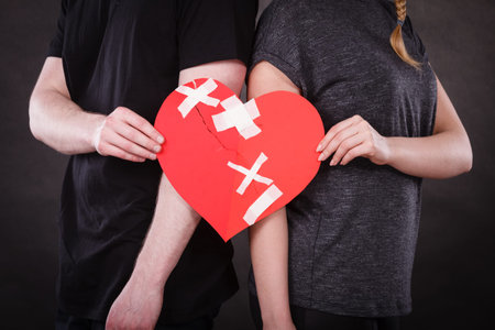 Broken heart difficult love concept. Couple woman and man hands holding paper red heart fixed with...