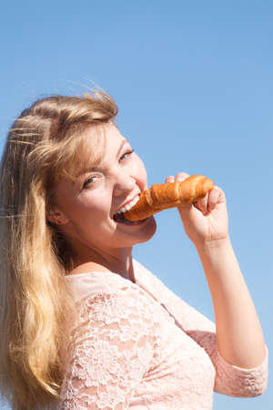 Young woman eating croissant meal food outdoor. Pretty girl having breakfast. Summer pleasure.の写真素材