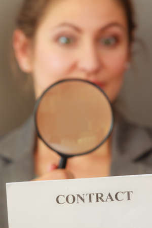 Contracts and agreements concept. Adult beauty woman in jacket holding showing contract. Close up portrait of person with loupe studying agreement.の写真素材