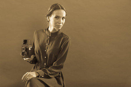 Woman retro style long dark gown taking picture with old camera, vintage photo