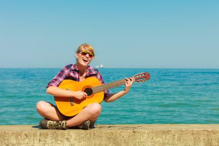 Music and people concept. Young woman traveller hiker with guitar outdoor on sea coast