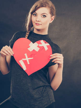 Healed love. Valentines Day concept. Young smiling woman holding big red heart with plaster. Girlfriend healing relationship.の写真素材
