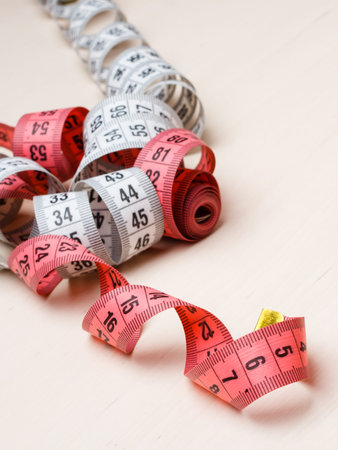 Two measure tapes red and white on wooden surface