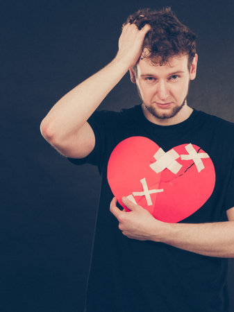 Separation and conflict. Young upset sad man with red heart glued by plaster. Guy lost his love...