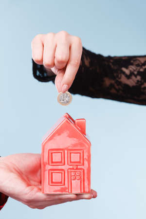 People hands with red little house piggy bank and silver coin.の写真素材