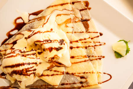 Pancake with ice cream and chocolate sauce on tableの写真素材