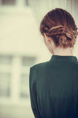 Alone woman looking through window waiting back view indoorの写真素材