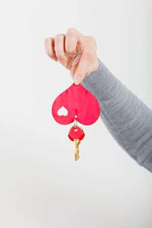 Woman hand holds little red heart with keys to new home house flat apartment.の写真素材