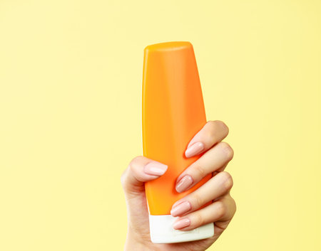Woman holding in hand sunscreen lotion, yellow backgroundの写真素材
