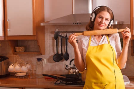 Happy relaxed beauty woman housewife chef with earphones listening music in house kitchen making dinner meal.の写真素材