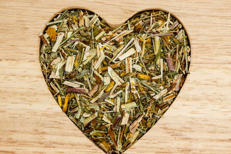 Dried herb leaves heart shaped on wooden surface. Herbaceous dry aromatic plant. Healthy cooking concept.の写真素材